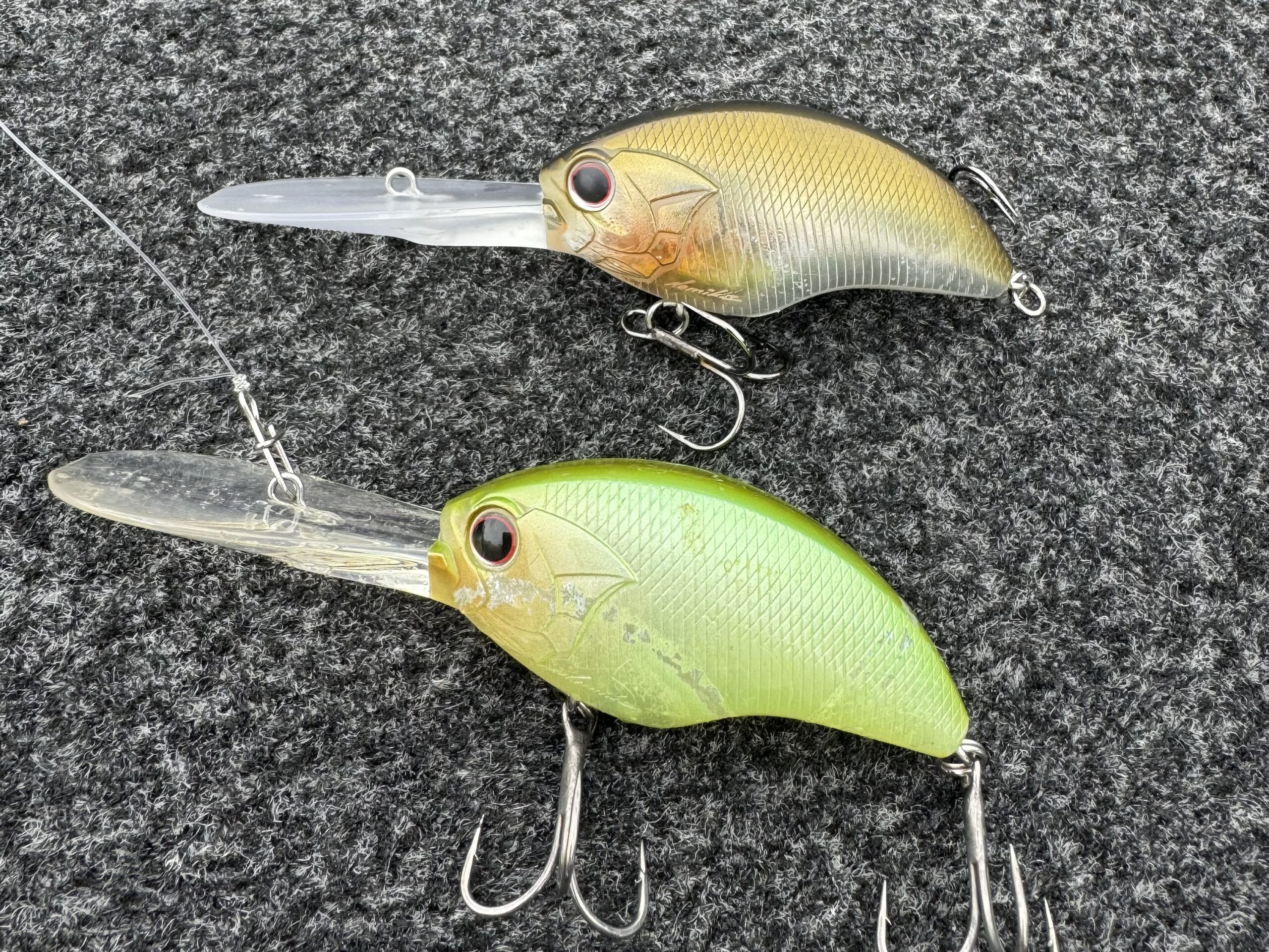 Two deep-diving crankbaits, gold and chartreuse, lying on a boat deck