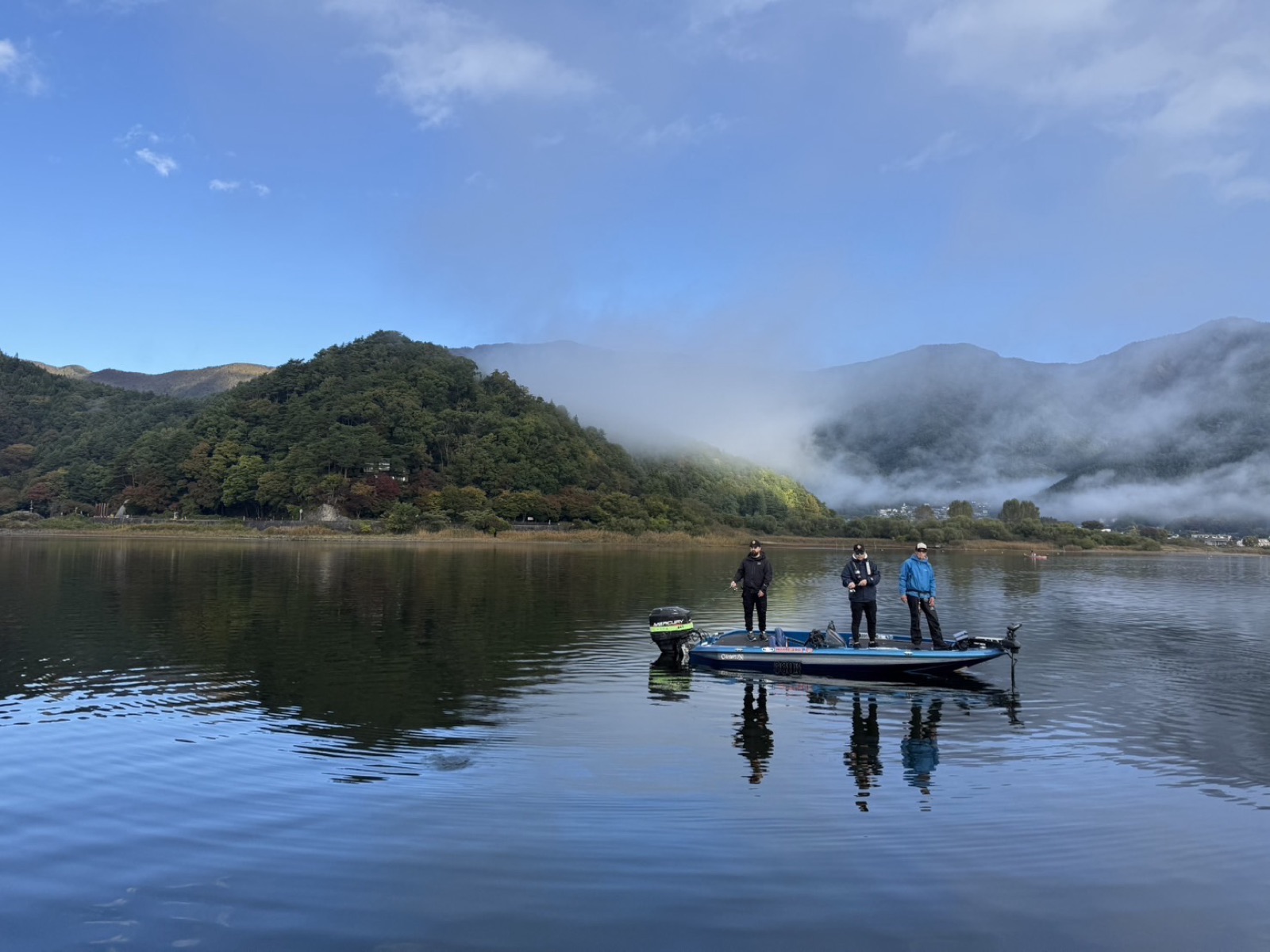 Morning mist over Lake Kawaguchi while anglers fish from a bass boat